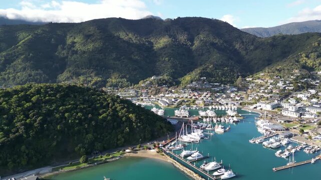 Aerial view of Picton port in New Zealand with yachts and ships moored along docks in Queen Charlotte Sound surrounded by beautiful urban coastal scenery for travel 