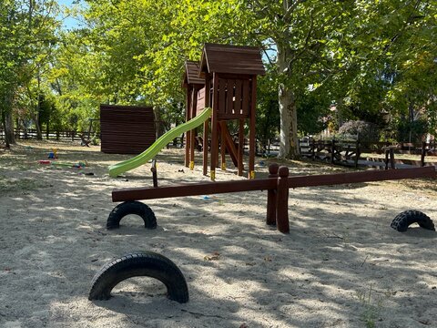 A long wooden seesaw on a playground sand with black rubber tires under the seats on a sunny day