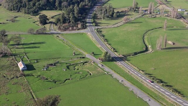 Beautiful aerial view of a road crossing a scenic New Zealand valley surrounded by expansive green fields, lush forests and stunning mountains in pristine nature for tourism 