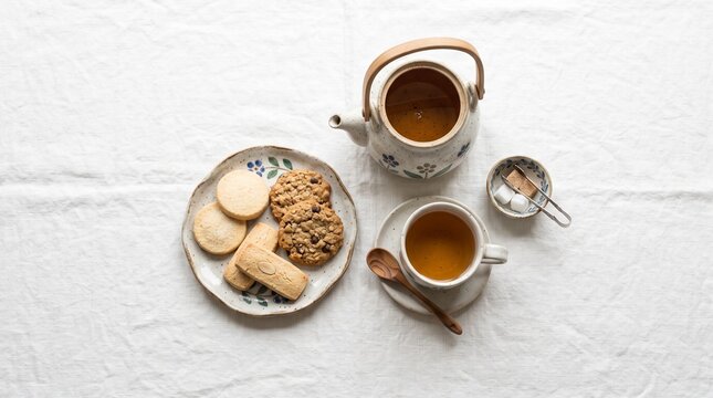 Afternoon Tea Break: A delightful spread of assorted cookies and biscuits rests on a rustic plate, accompanied by a steaming teapot and a cup of warm tea, perfect for a tranquil afternoon respite.