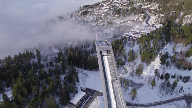 Close up aerial view of top of Holmenkollen ski jump structure with fog covered snowy village in background, Norway