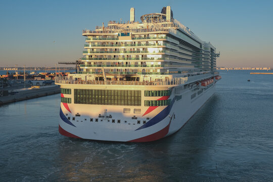 Massive gigantic modern cruiseship cruise ship liner Iona or Arvia in Cadiz, Spain during summer Mediterranean cruising with harbor and container port infrastructure