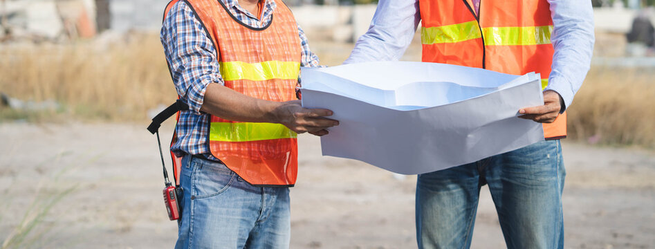 Two engineers discussing on blueprint of project.