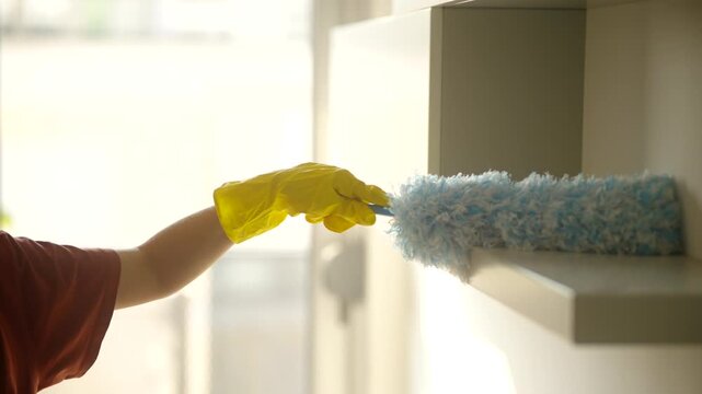 Housekeeper Dusting White Shelf With Blue Microfiber Duster During Home Cleaning Routine