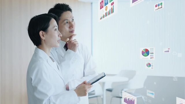 会話する白衣の男女と統計データ。科学、医療、医師、実験、調査、検査、分析、病院、診断、経営、管理