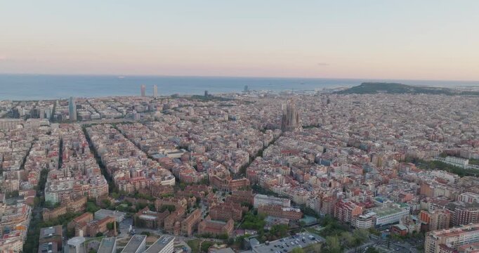 Cinematic aerial of Barcelona city skyline. Drone fly over Eixample residential famous urban grid and Sagrada Familia cathedral with morning sunrise cityscape. Catalonia, Spain. Travel Destination.