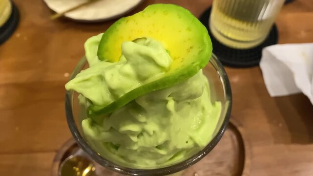 Avocado smoothie with ice cream topping horizontal video, traditional Vietnamese kem bo dessert with fresh avocado slice close up in cafe