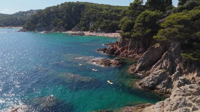 An aerial view of a drone flies over the beach, sea and coastal cliffs near Santa Clotilde Park on a sunny day in the tourist town of Lloret de Mar, Catalonia, Spain