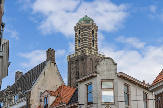 Zwolle, Netherlands: View of the famous Peperbus (Onze Lieve Vrouwetoren) church tower rising above traditional historic brick houses and rooftops under a blue sky with clouds.