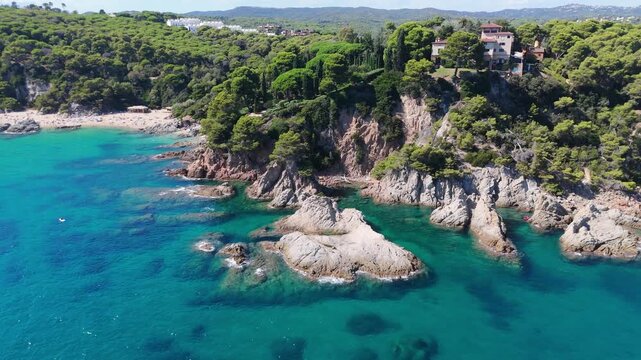 An aerial view of a drone flies over the beach, sea and coastal cliffs near Santa Clotilde Park on a sunny day in the tourist town of Lloret de Mar, Catalonia, Spain