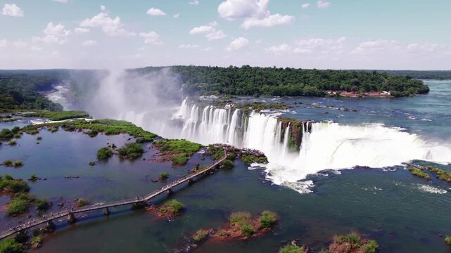 4K drone aerial view of Devil&rsquo;s Throat at Iguazu Falls on the Argentina-Brazil border. The iconic waterfall plunges through the rainforest, with walkways extending toward the spectacular viewpoint.