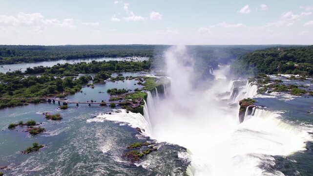 4K drone aerial view of Devil&rsquo;s Throat at Iguazu Falls on the Argentina-Brazil border. The iconic waterfall plunges through the rainforest, with walkways extending toward the spectacular viewpoint.