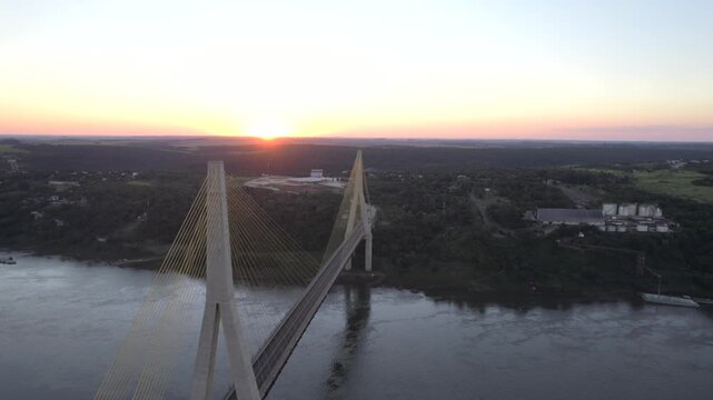 4K drone aerial view of the Integration Bridge at sunset, connecting Paraguay and Brazil across the Paran&aacute; River near the Triple Frontier. Warm evening light illuminates the bridge and surrounding lan