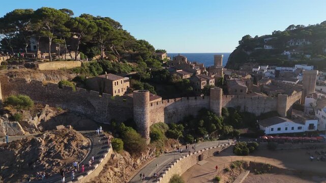Aerial drone view of a fortress on coastal cliffs, a beach and the sea at sunset in the tourist town of Tossa de Mar, Catalonia, Spain