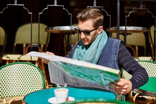 Man, travel and map at outdoor cafe for destination, sightseeing or directions to location. Male person, tourist guide and reading information at coffee shop with drink, itinerary or planning trip