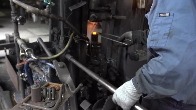 Factory worker in blue uniform operating a hot forging press machine
