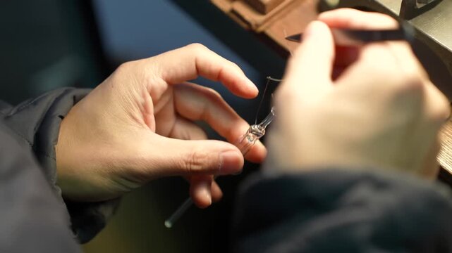 Close up of hands positioning thin filament wires on a glass bulb mount