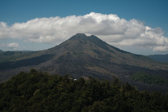 Mount Batur volcano with black lava fields and forest under a blue sky, Kintamani, Bali, Indonesia