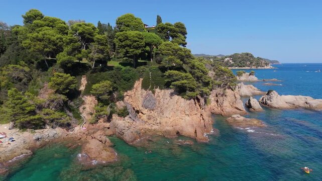 An aerial view of a drone flies over the beach, sea and coastal cliffs near Santa Clotilde Park on a sunny day in the tourist town of Lloret de Mar, Catalonia, Spain