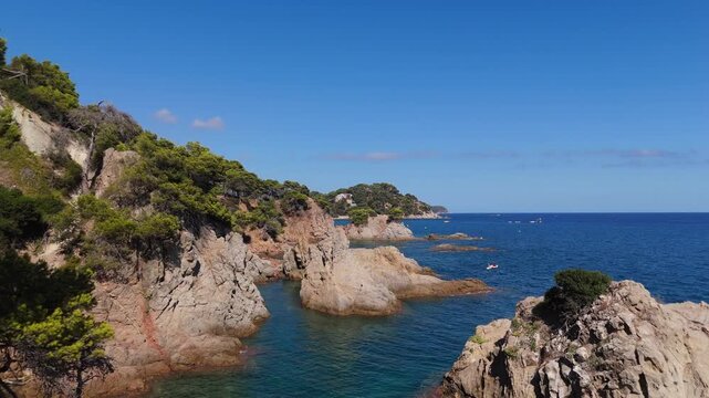 An aerial view of a drone flies over the beach, sea and coastal cliffs near Santa Clotilde Park on a sunny day in the tourist town of Lloret de Mar, Catalonia, Spain