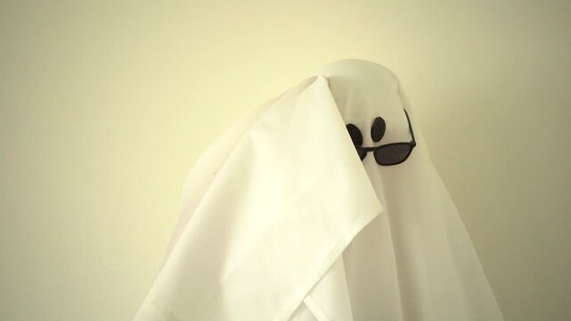 Playful and sassy Halloween ghost wearing sunglasses showing different emotions, simple studio portrait with copy space, spooky, funny and seasonal concept.