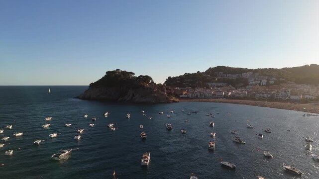 An aerial view of a drone flying over a bay with moored boats and yachts at sunset in the tourist town of Tossa De Mar, Catalonia, Spain