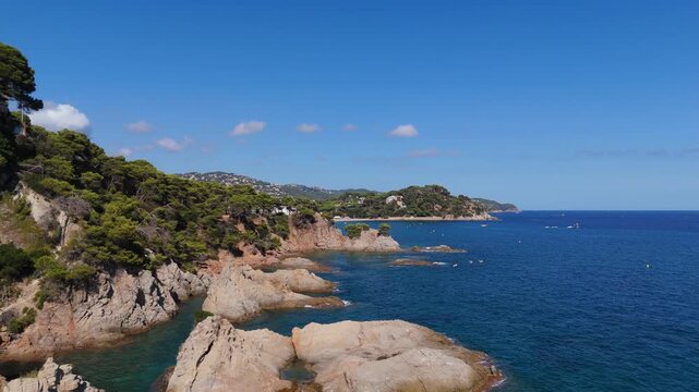 An aerial view of a drone flies over the beach, sea and coastal cliffs near Santa Clotilde Park on a sunny day in the tourist town of Lloret de Mar, Catalonia, Spain