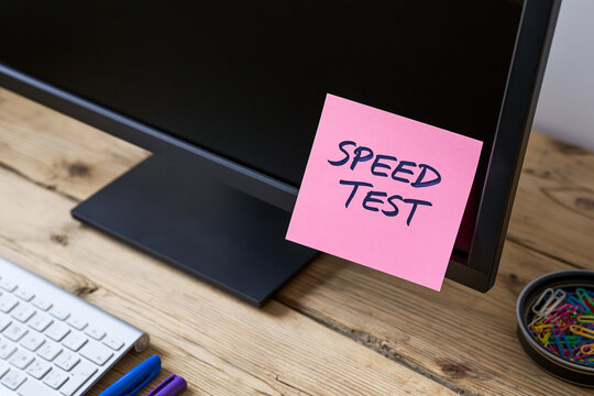 A pink sticky note with speed test written on it is attached to a computer monitor.