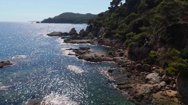 An aerial view of a drone flies over the beach, sea and coastal cliffs near Santa Clotilde Park on a sunny day in the tourist town of Lloret de Mar, Catalonia, Spain