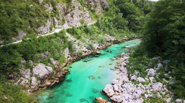 Aerial drone view of the turquoise river with white boulders and a footpath along the rocky bank, Soca Valley, Slovenia