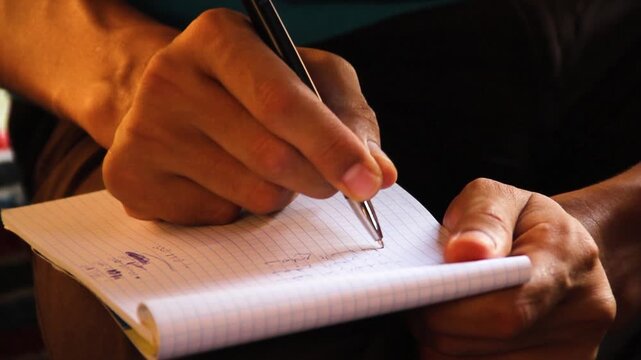 A close-up shot of a person's hands writing notes in a lined notebook with a black pen, capturing the focus and detail of the writing process.