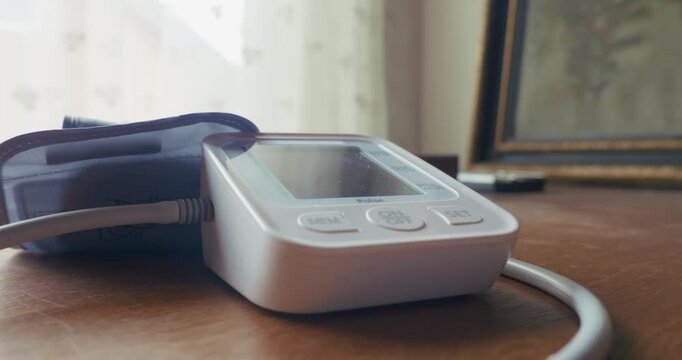 Side view close up of a home patient pressing the power button on a digital blood pressure monitor. Captures daily health tracking, hypertension checks, and personal healthcare routines.
