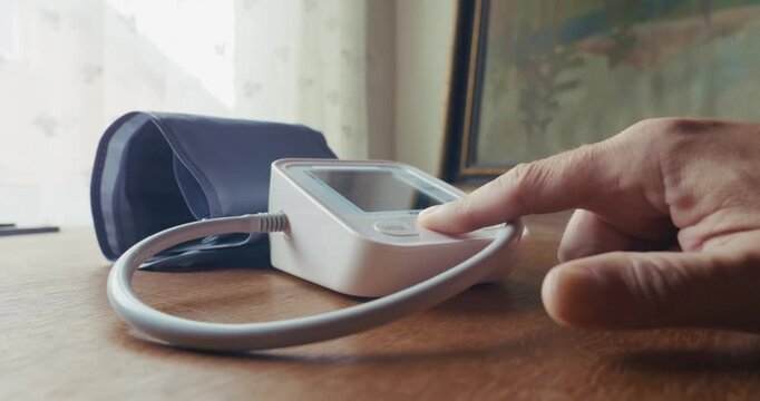 Close-up of a home patient placing a blood pressure armband and digital monitoring device on a table after completing a routine personal check.
