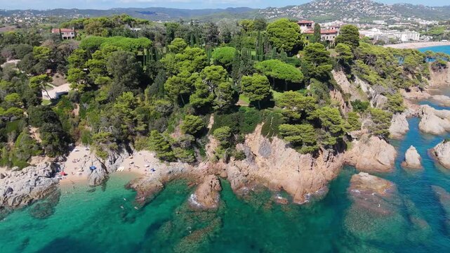An aerial view of a drone flies over the beach, sea and coastal cliffs near Santa Clotilde Park on a sunny day in the tourist town of Lloret de Mar, Catalonia, Spain