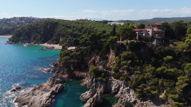An aerial view of a drone flies over the beach, sea and coastal cliffs near Santa Clotilde Park on a sunny day in the tourist town of Lloret de Mar, Catalonia, Spain