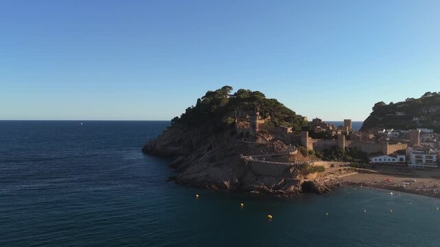 Aerial drone view of a fortress on coastal cliffs, a beach and the sea at sunset in the tourist town of Tossa de Mar, Catalonia, Spain