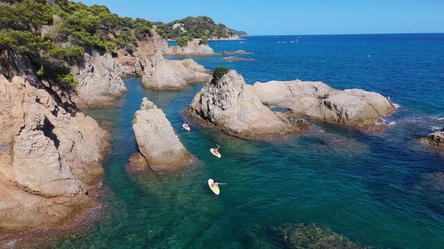 An aerial view of a drone flies over the beach, sea and coastal cliffs near Santa Clotilde Park on a sunny day in the tourist town of Lloret de Mar, Catalonia, Spain