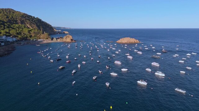 An aerial view of a drone flying over a bay with moored boats and yachts at sunset in the tourist town of Tossa De Mar, Catalonia, Spain
