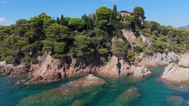An aerial view of a drone flies over the beach, sea and coastal cliffs near Santa Clotilde Park on a sunny day in the tourist town of Lloret de Mar, Catalonia, Spain