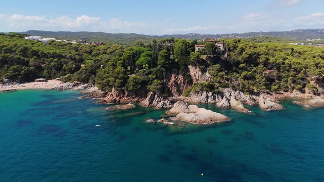 An aerial view of a drone flies over the beach, sea and coastal cliffs near Santa Clotilde Park on a sunny day in the tourist town of Lloret de Mar, Catalonia, Spain