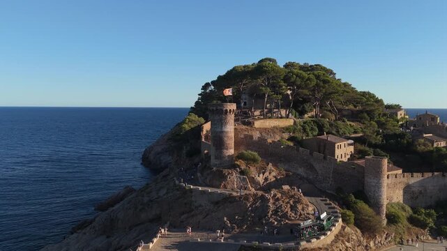 Aerial drone view of a fortress on coastal cliffs, a beach and the sea at sunset in the tourist town of Tossa de Mar, Catalonia, Spain