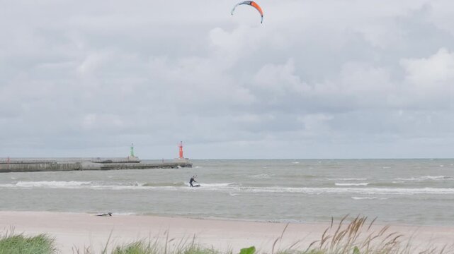 Kitesurfer riding waves on cloudy day near sea pier