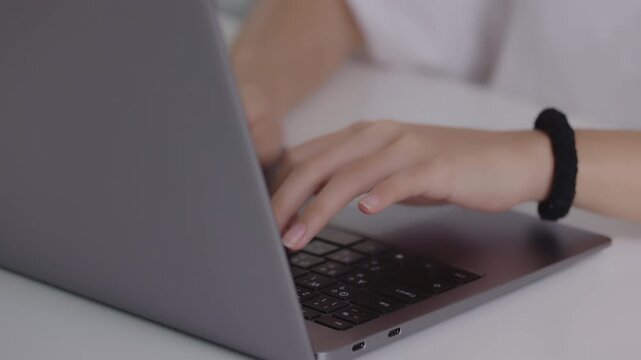 Close-up shot of female hands typing on a laptop keyboard at a white desk, ideal for concepts of remote work, online business, data entry, and technology.