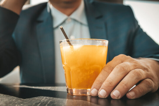man hold in hand yellow orange refreshment exotic juice with straw on wooden table. business lunch. A businessman drinks a cocktail at bar.