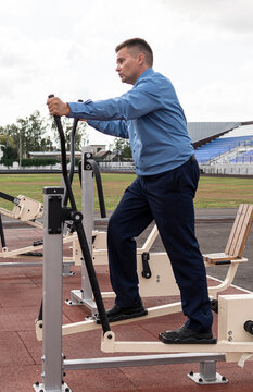 man in a business suit is warming up on simulators at the stadium. Sports exercises after office work. The fight against excess weight. Businessman in the gym.