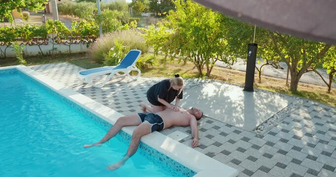 Woman performing CPR and attempting to revive an unconscious man beside a swimming pool after a water accident, representing drowning rescue and emergency first aid.