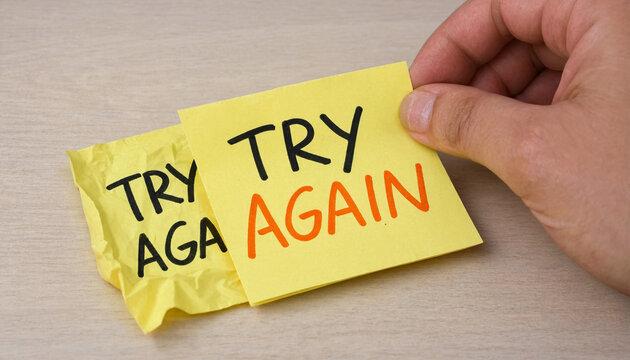 Hand holding yellow sticky note with try again text concept for perseverance and motivation on wooden surface