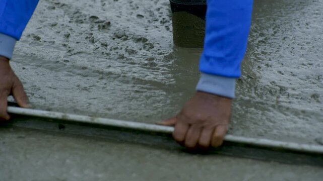 Worker Screeding Wet Concrete In Rubber Boots