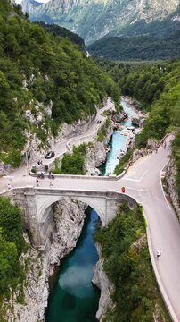 Vertical aerial drone view of the stone Napoleon Bridge and the mountain road above the emerald river in its narrow gorge, Kobarid, Slovenia