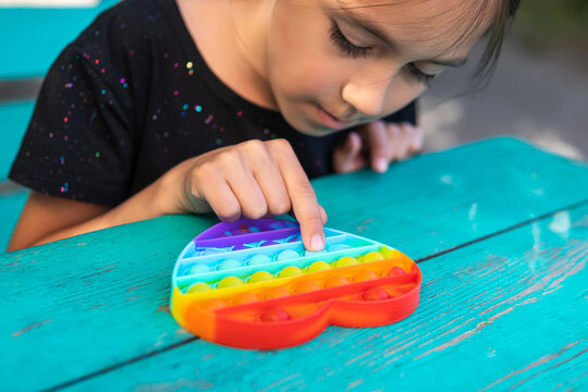 Cute faceless child playing with the Pop It fidget. girl looks at the toy. Selective focus on toy.